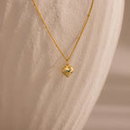 Gold Puff Heart Pendant Necklace displayed against a textured, ivory-toned background.