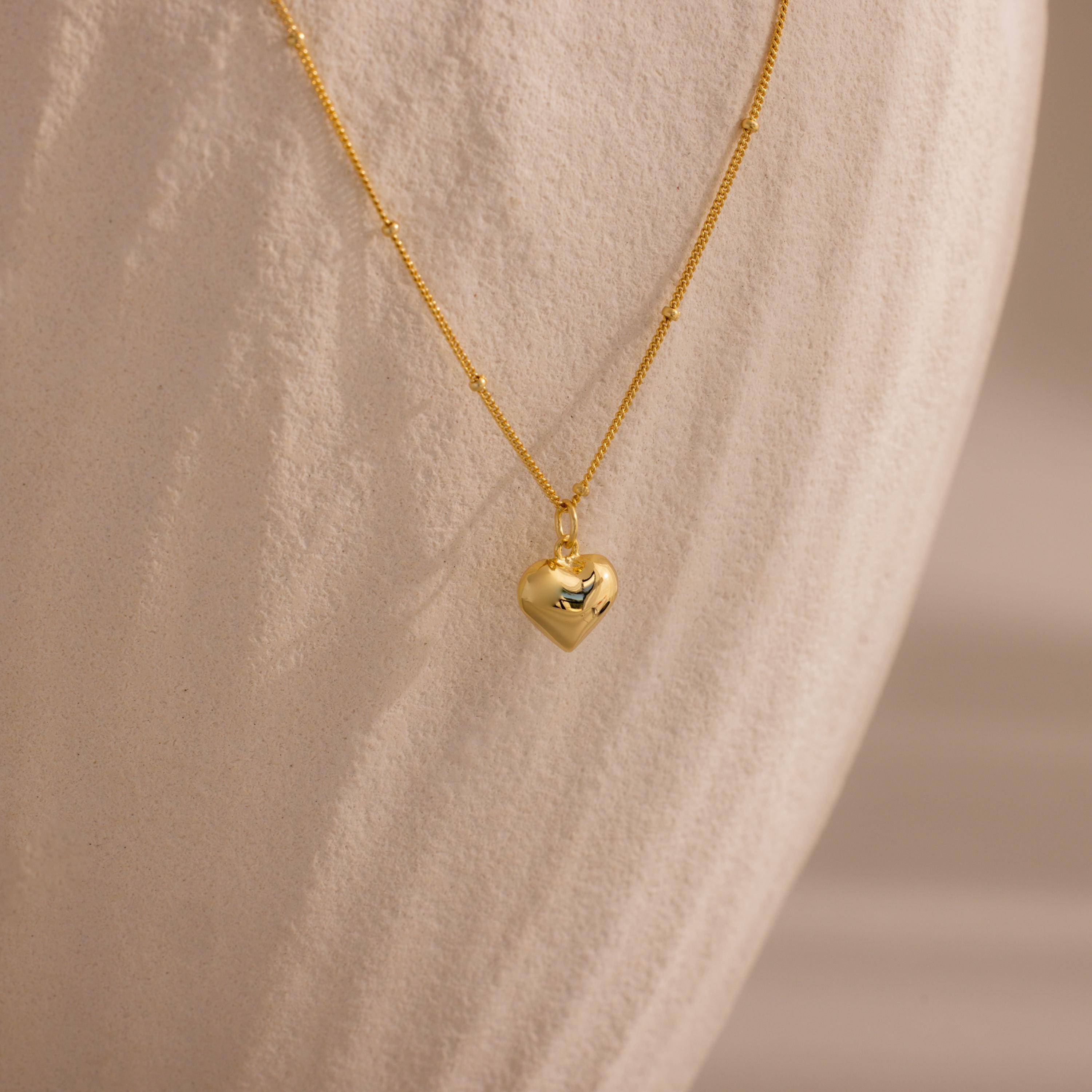 Gold Puff Heart Pendant Necklace displayed against a textured, ivory-toned background.