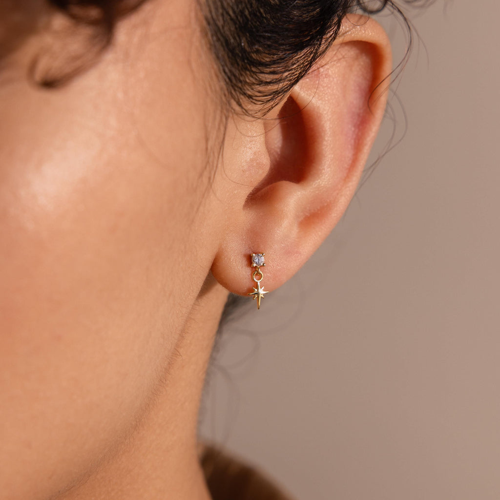 A model wears one 18k gold Diamond Star Flatback Earring on her earlobe, showcasing how the charm dangles just below the gemstone stud.