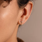 A model wears one 18k gold Diamond Star Flatback Earring on her earlobe, showcasing how the charm dangles just below the gemstone stud.