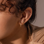 A close-up of a model’s ear adorned with layered earrings, including the 18k gold Diamond Star Flatback Earring in the second piercing hole, styled next to a small hoop and a tiny stud.