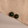 Pair of green jade rose earrings with faceted center stones displayed on a torn-edge neutral fabric background.