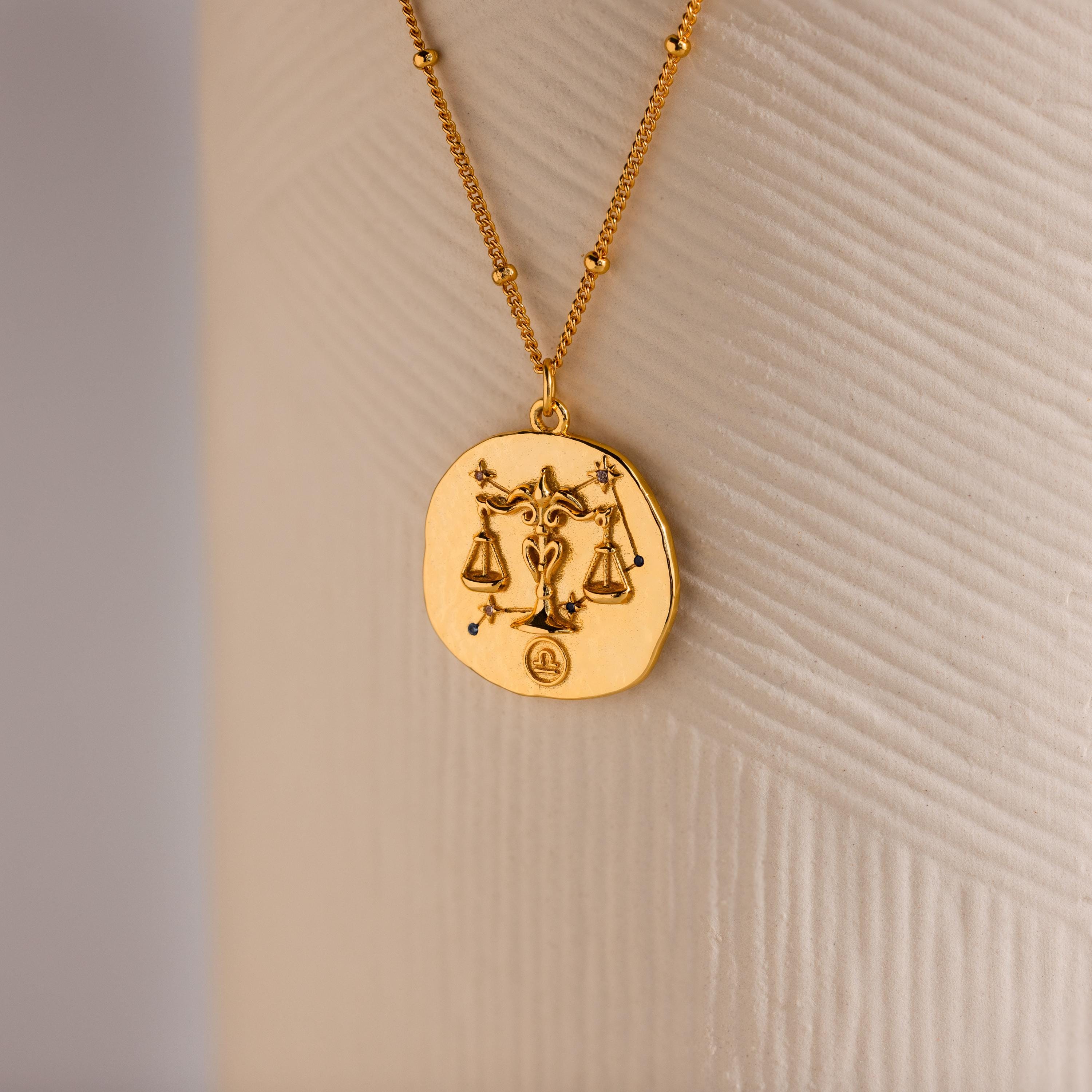 Close up of a Gold 3D Libra Zodiac Coin Pendant Necklace with small CZ gemstones, attached to a dainty satellite chain.