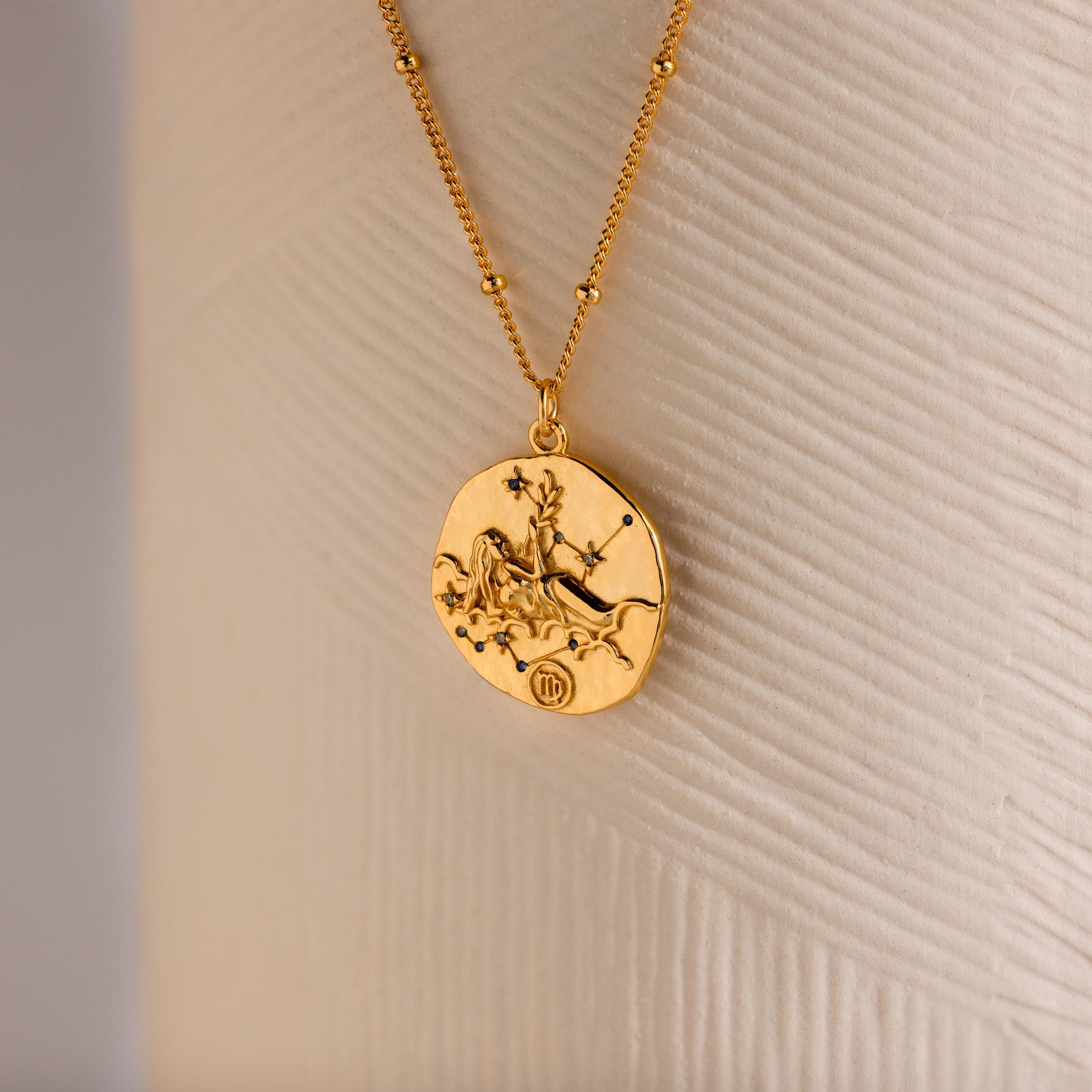 Close up of a Gold 3D Virgo Zodiac Coin Pendant Necklace with small CZ gemstones, attached to a dainty satellite chain.