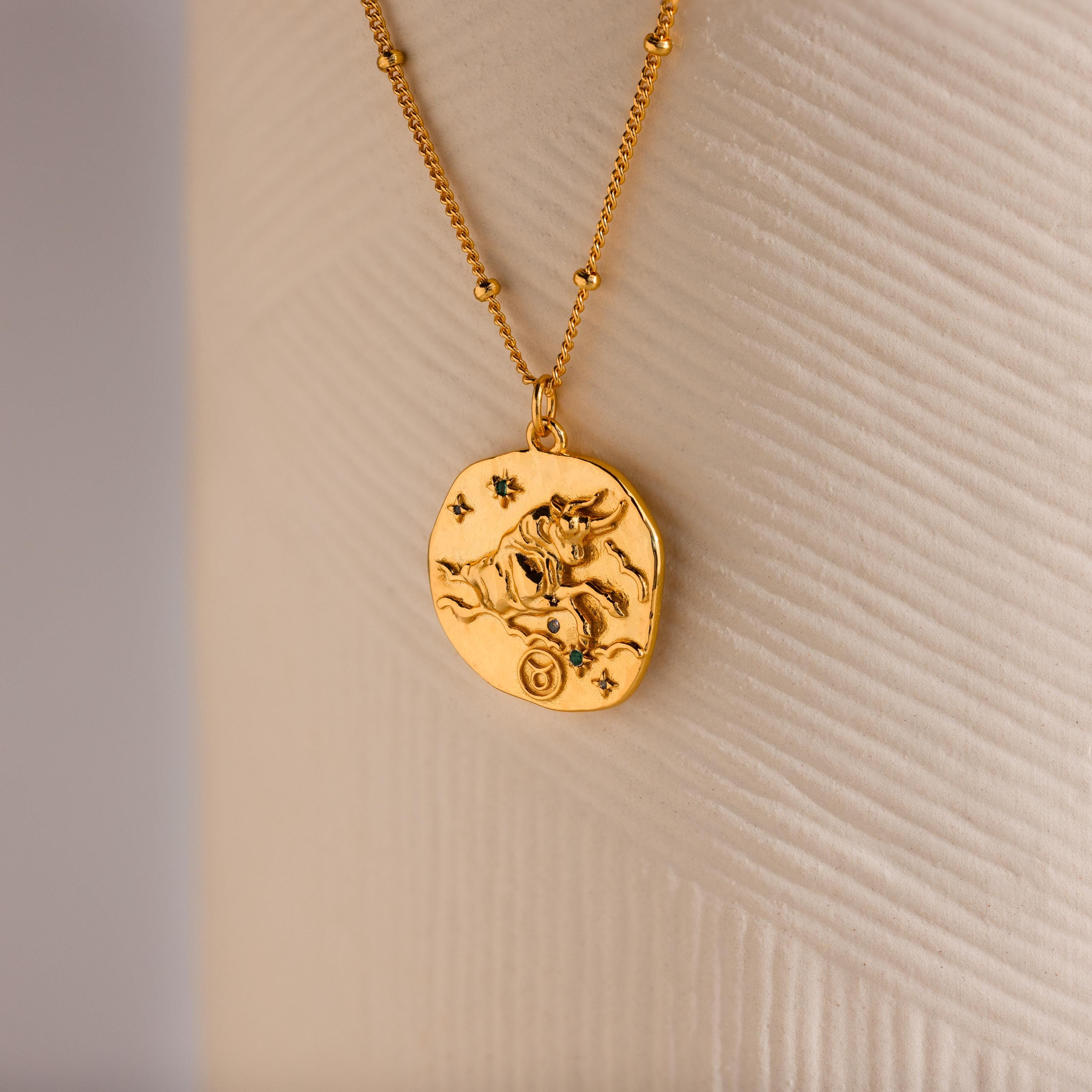 Close up of a Gold 3D Taurus Zodiac Coin Pendant Necklace with small CZ gemstones, attached to a dainty satellite chain.