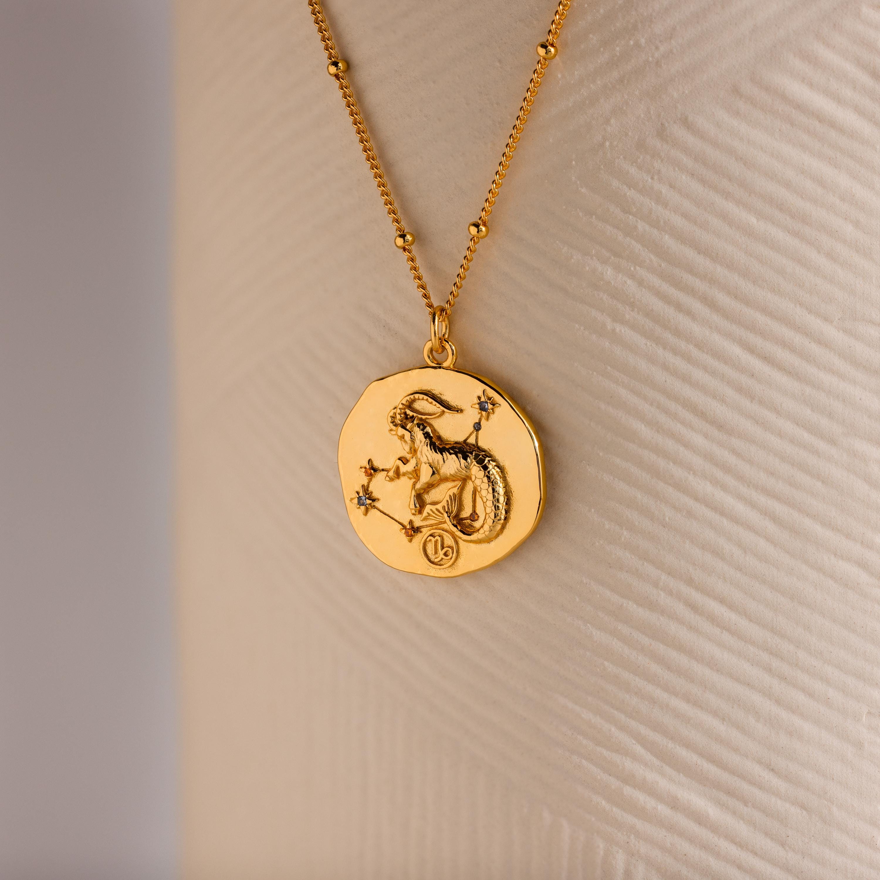 Close up of a Gold 3D Capricorn Zodiac Coin Pendant Necklace with small CZ gemstones, attached to a dainty satellite chain.