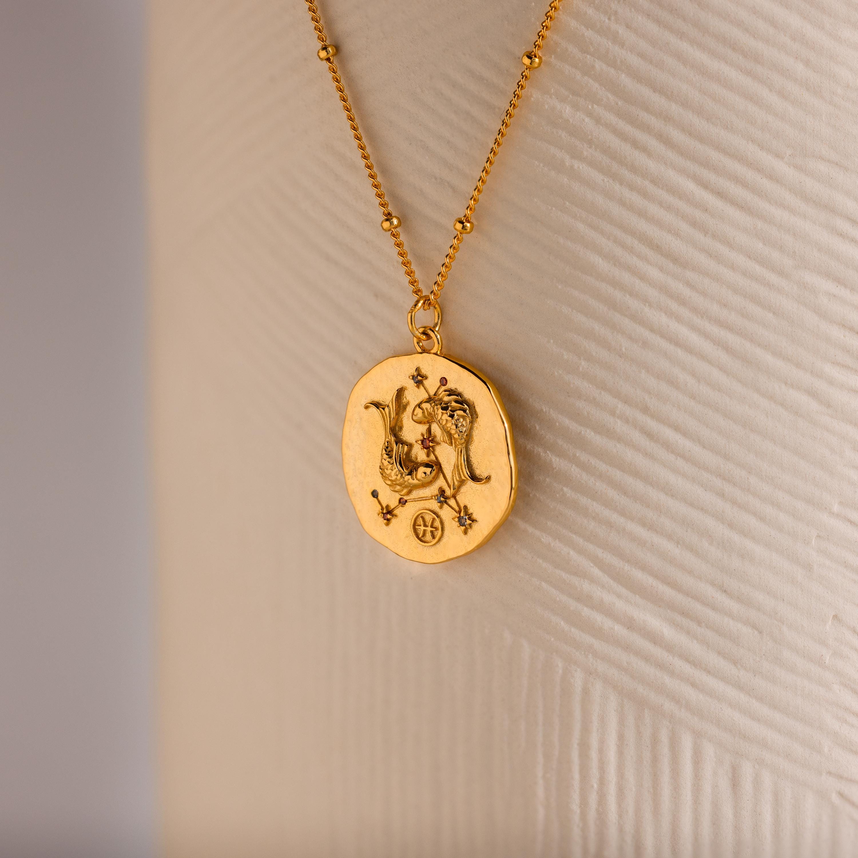 Close up of a Gold 3D Pisces Zodiac Coin Pendant Necklace with small CZ gemstones, attached to a dainty satellite chain.