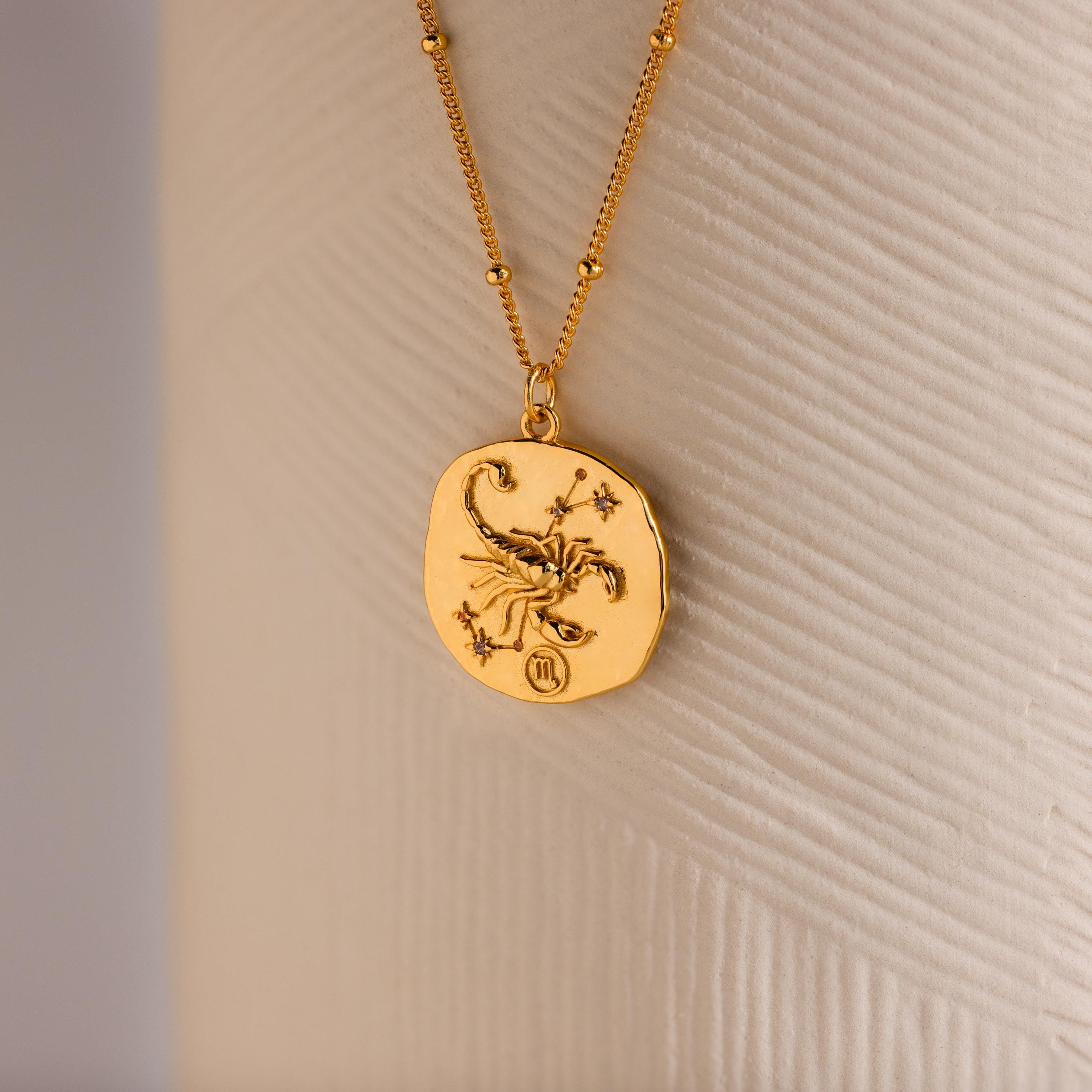 Close up of a Gold 3D Scorpio Zodiac Coin Pendant Necklace with small CZ gemstones, attached to a dainty satellite chain.