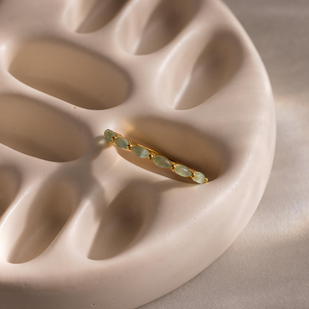 Marquise jade ring laid flat on a sculptural beige ceramic tray, with the soft curves of the dish adding texture to the composition.