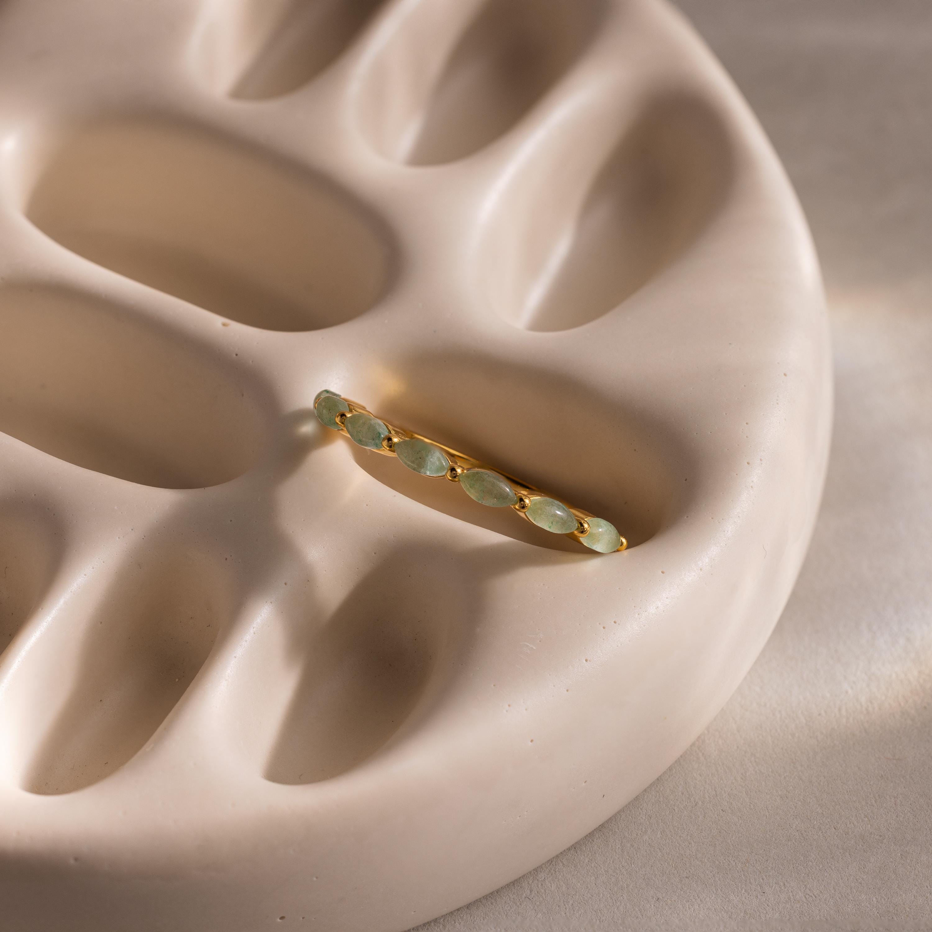 Marquise jade ring laid flat on a sculptural beige ceramic tray, with the soft curves of the dish adding texture to the composition.