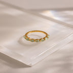 Minimalist product shot of a marquise-cut jade ring set in a slim gold band, displayed on a clear acrylic platform with soft shadows.