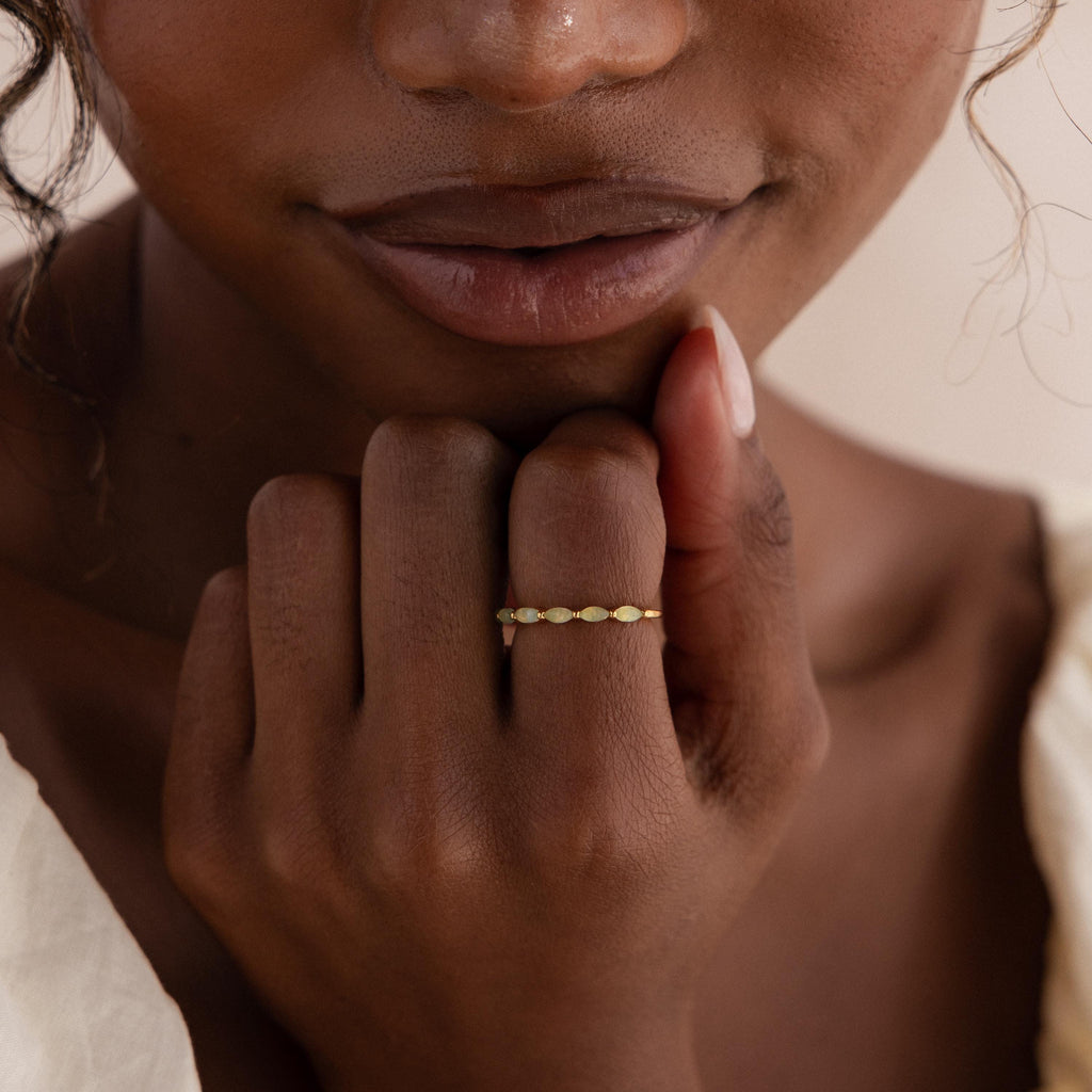A woman gently resting her hand near her face, wearing a delicate marquise jade ring in a gold band that complements her natural makeup.