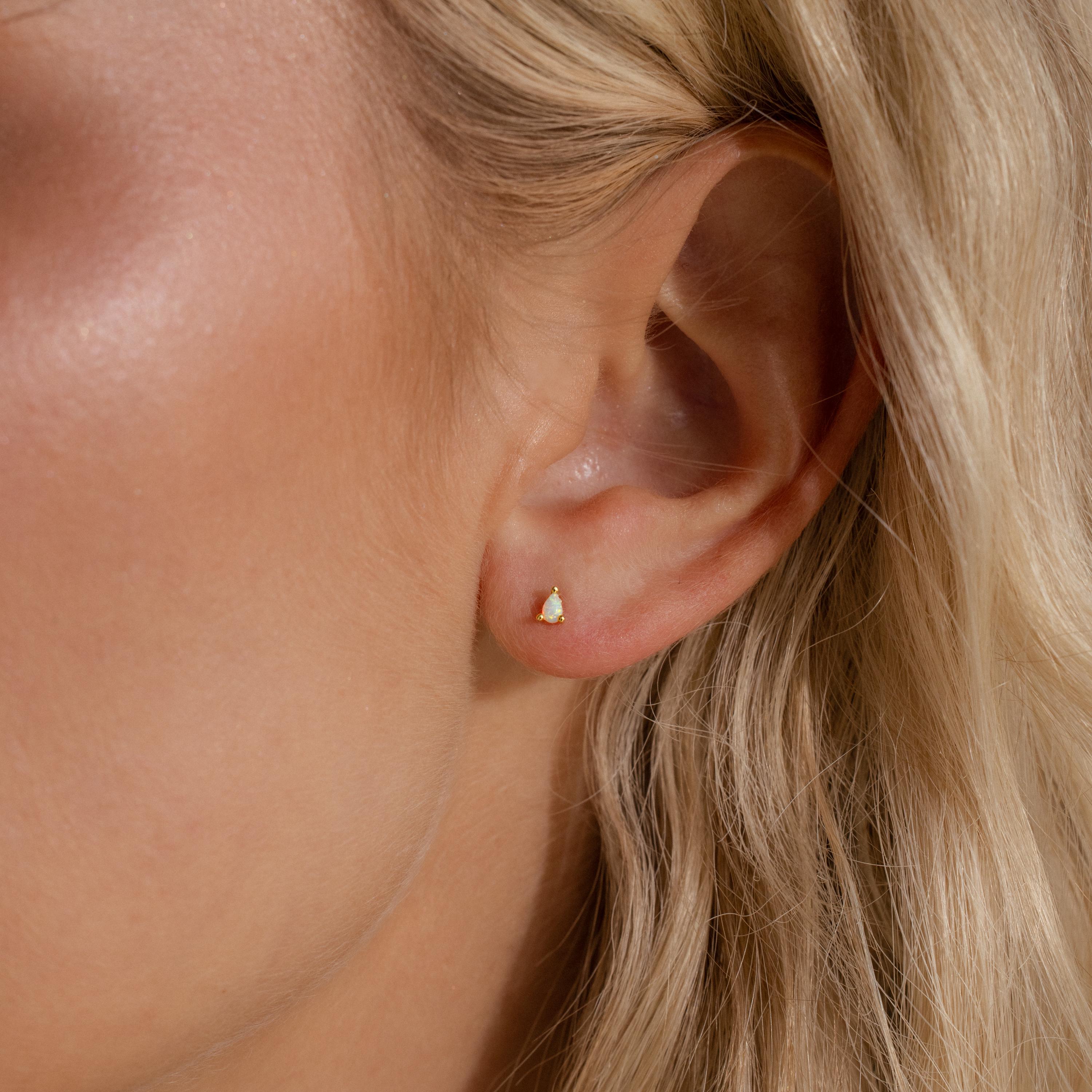 A gold pear opal stud worn on a woman’s earlobe, subtly catching the light for a soft, iridescent glow.