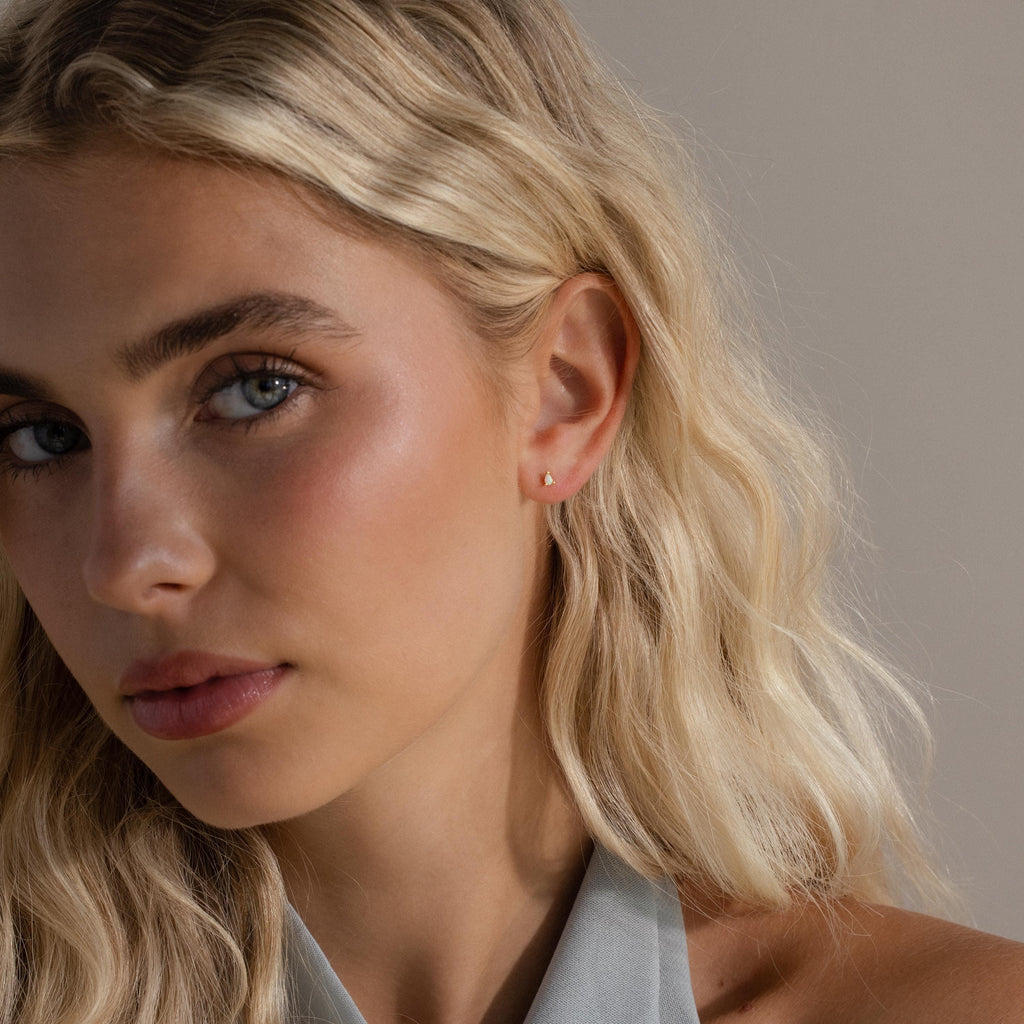 A model wearing a gold pear opal stud, captured in soft lighting that accentuates the opal's iridescence.