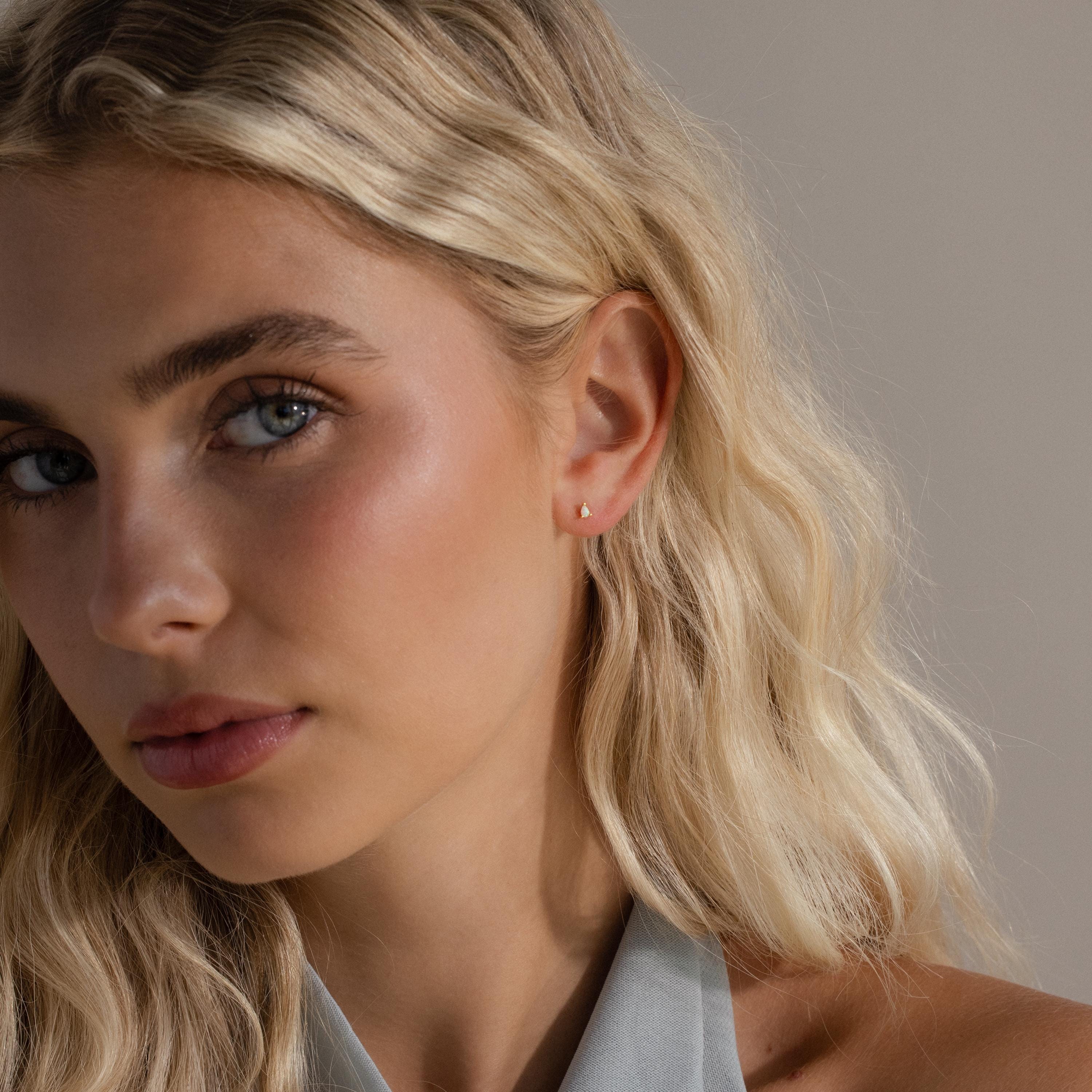 A model wearing a gold pear opal stud, captured in soft lighting that accentuates the opal's iridescence.
