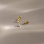 Two gold pear opal studs shown disassembled to reveal the flatback threading design on a minimalist beige surface.