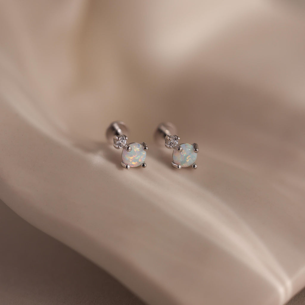 Pair of silver flat back earrings with opal centers and diamond accents on a satin background.