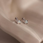 Pair of silver flat back earrings with opal centers and diamond accents on a satin background.