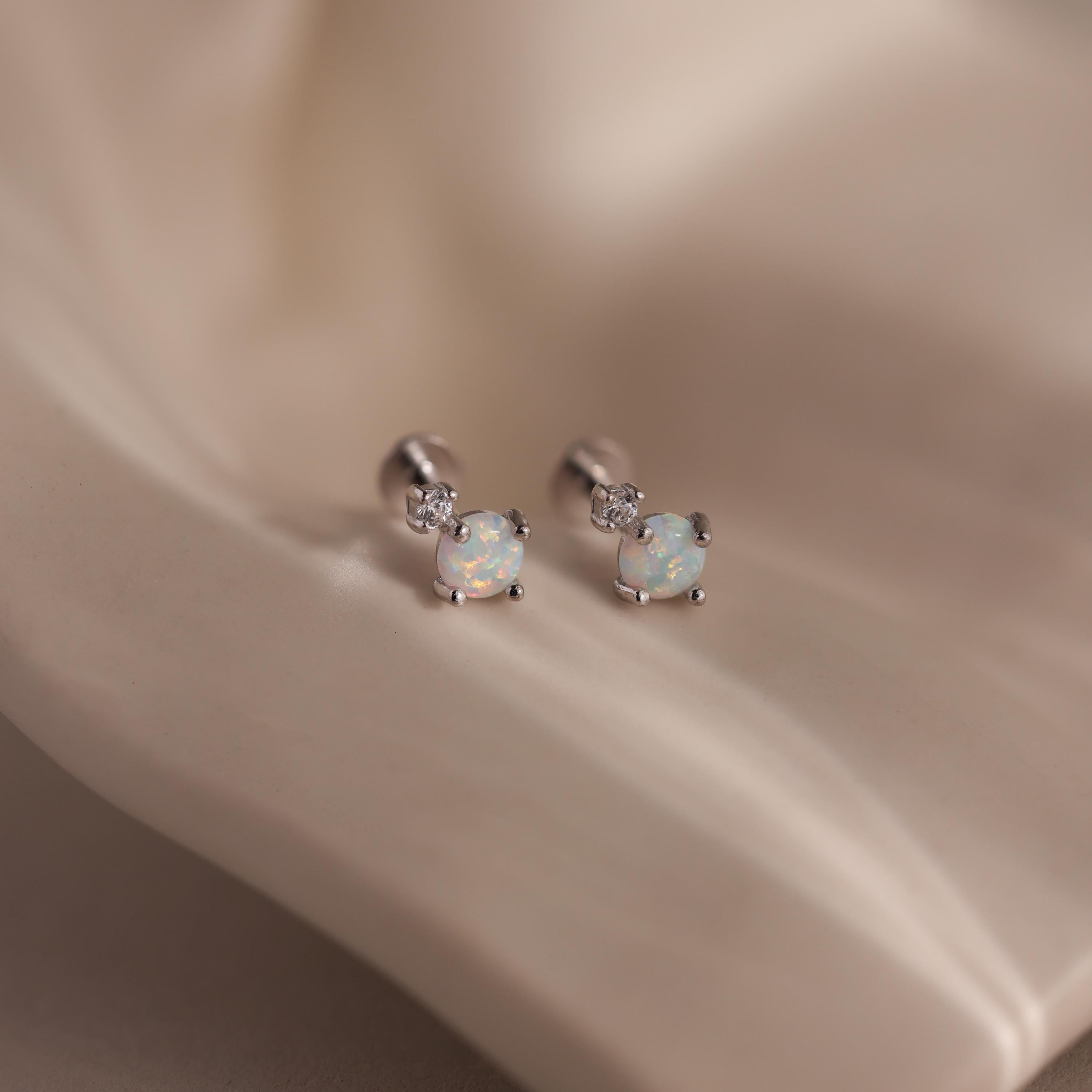 Pair of silver flat back earrings with opal centers and diamond accents on a satin background.