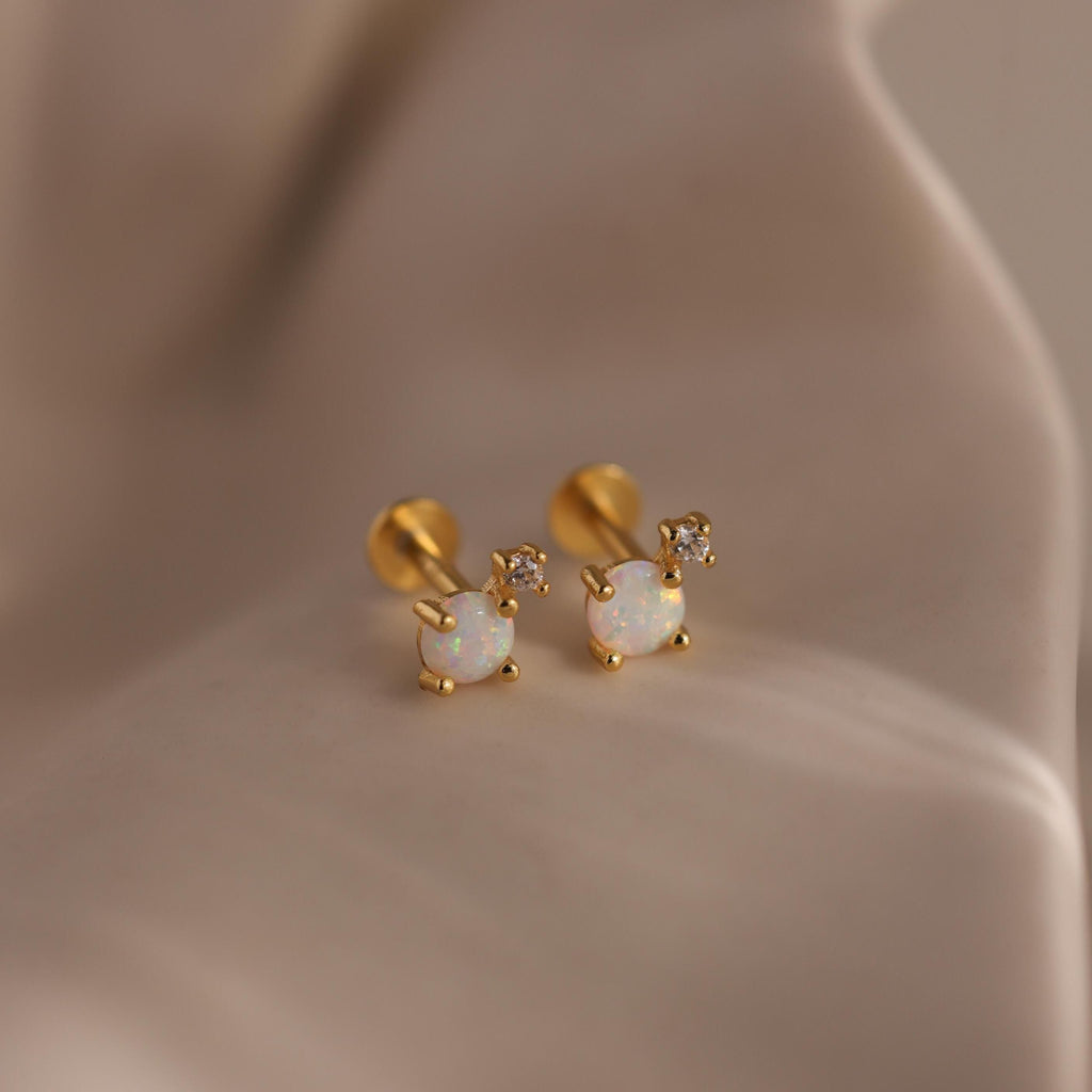 Pair of gold flat back opal and diamond earrings resting on a silky beige surface.