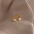 Pair of gold flat back opal and diamond earrings resting on a silky beige surface.