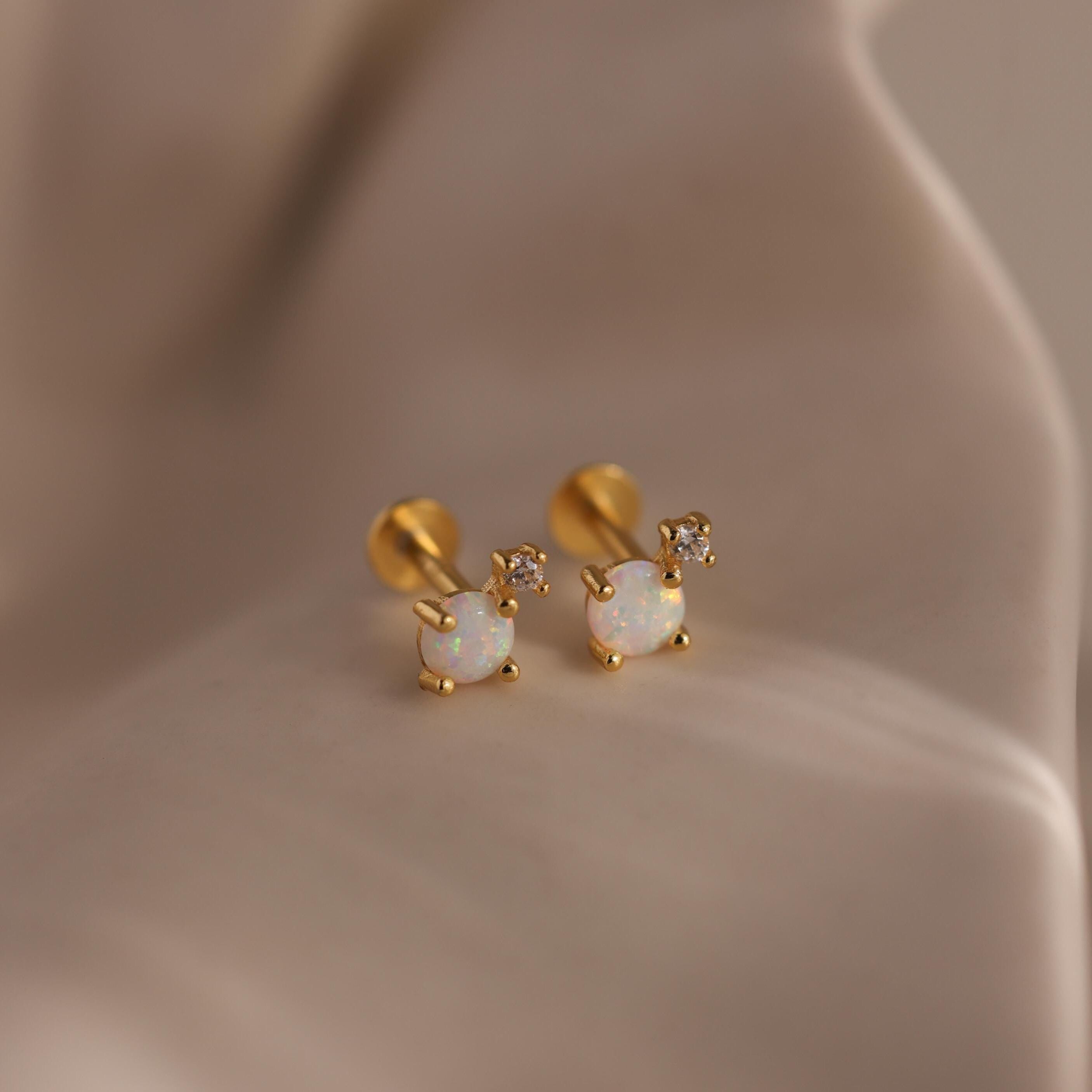Pair of gold flat back opal and diamond earrings resting on a silky beige surface.