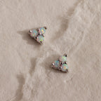 A pair of silver Opal Cluster Stud Earrings resting on a white textured paper, with a triangular trio of luminous white opals set in polished silver.