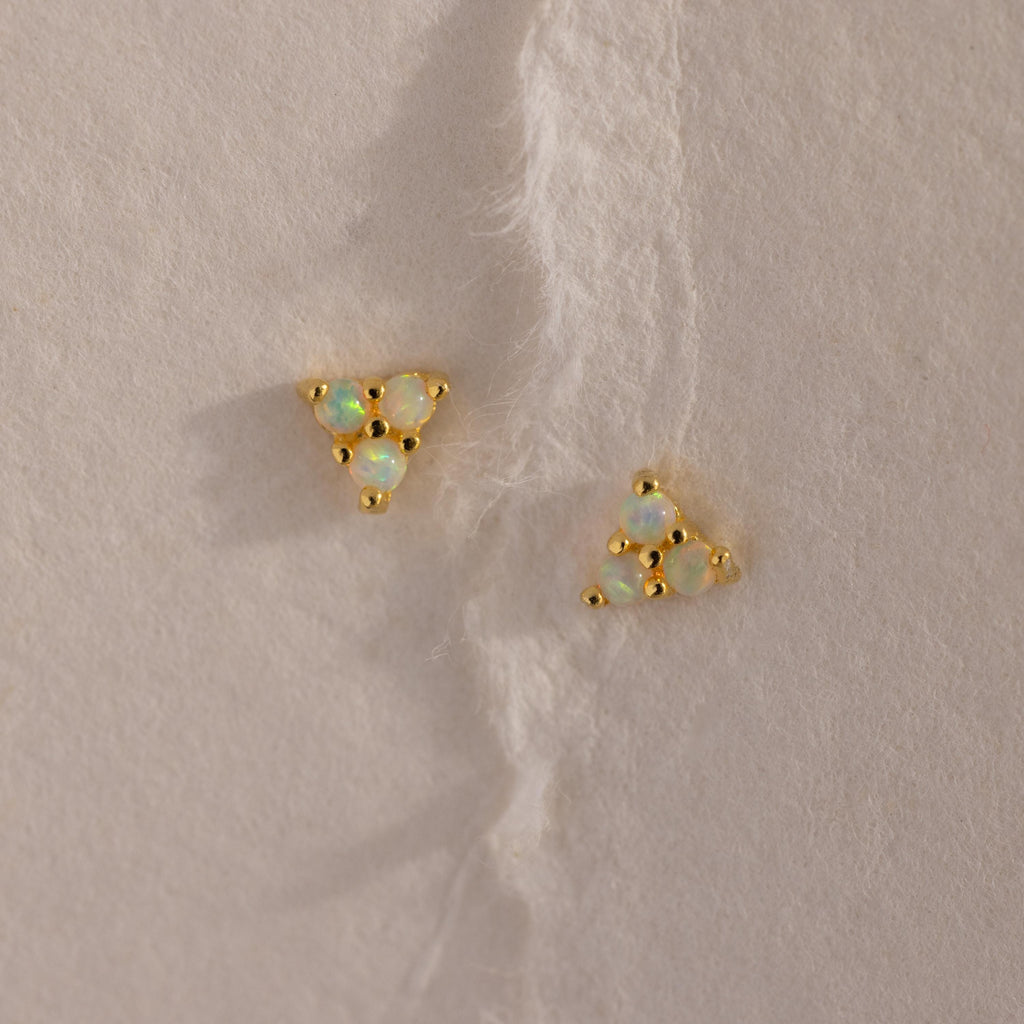 Two gold Opal Cluster Stud Earrings placed on a textured cream paper background, showcasing the triangle arrangement of luminous opals.