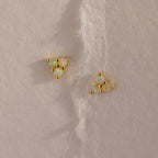 Two gold Opal Cluster Stud Earrings placed on a textured cream paper background, showcasing the triangle arrangement of luminous opals.