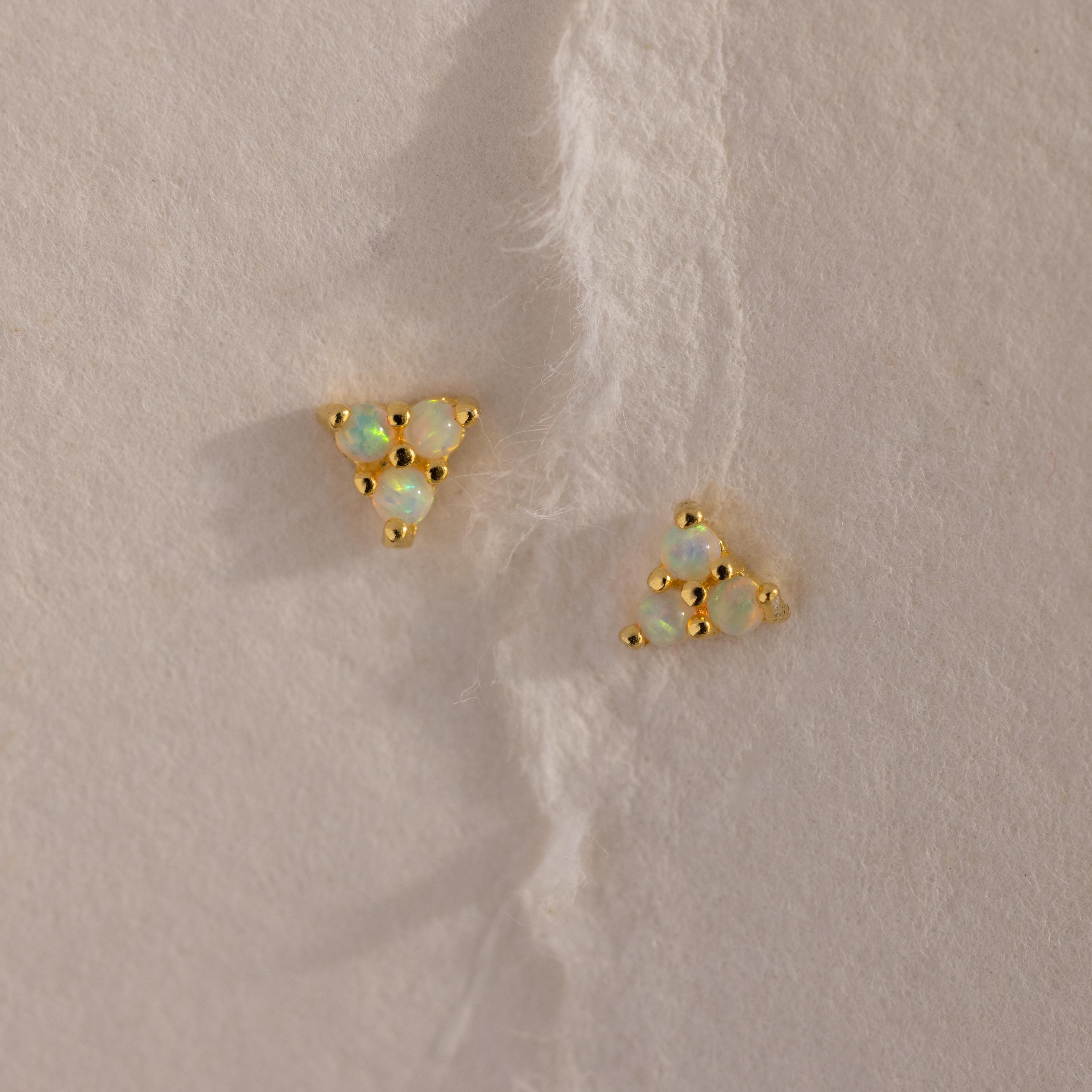 Two gold Opal Cluster Stud Earrings placed on a textured cream paper background, showcasing the triangle arrangement of luminous opals.