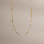 The Dainty Bow Necklace laid flat on a neutral surface, showing its full length, gold chain, and petite bow details.
