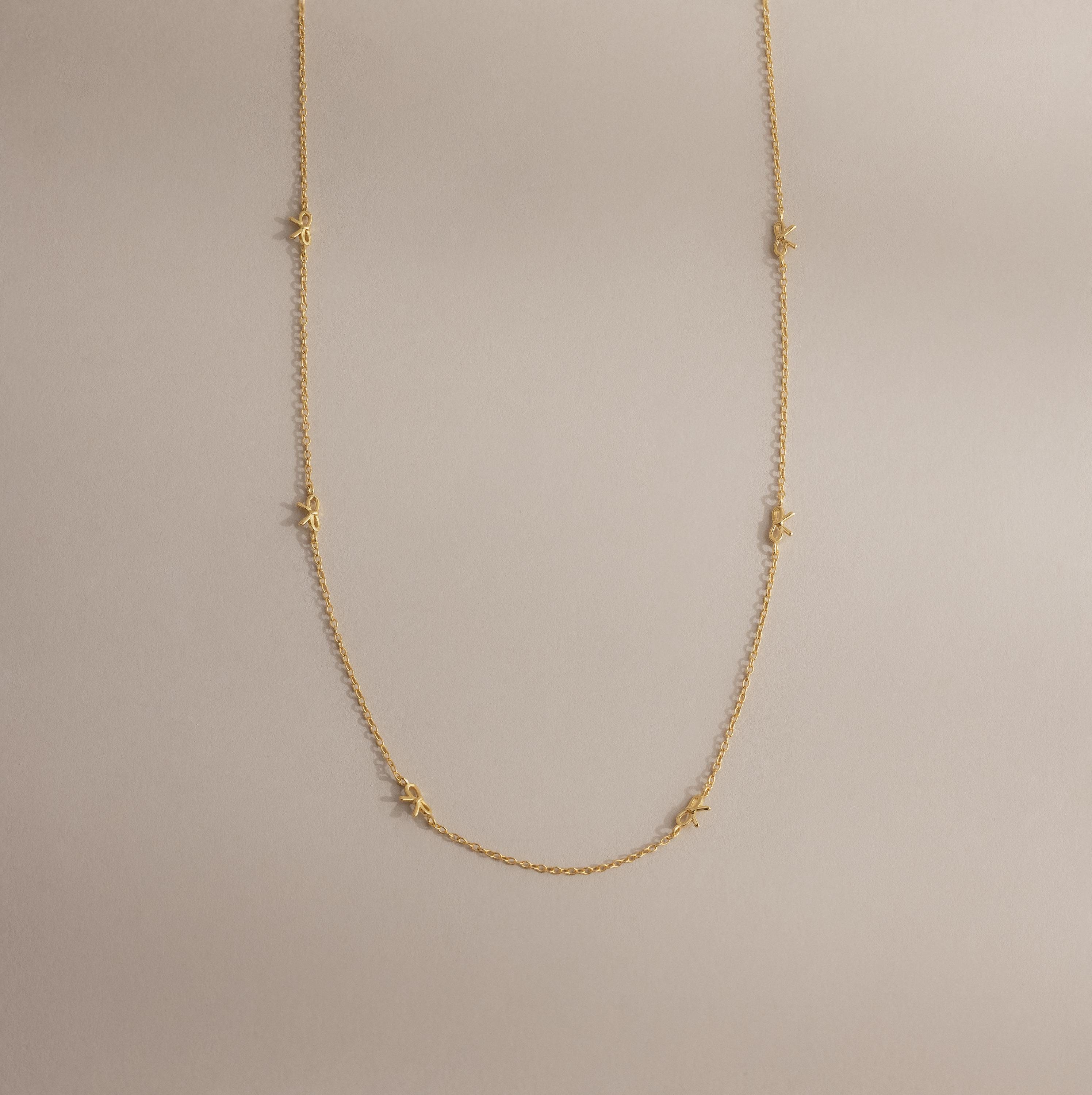 The Dainty Bow Necklace laid flat on a neutral surface, showing its full length, gold chain, and petite bow details.