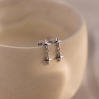 A pair of silver flat back earrings with double star drops hanging from a smooth, curved ceramic surface