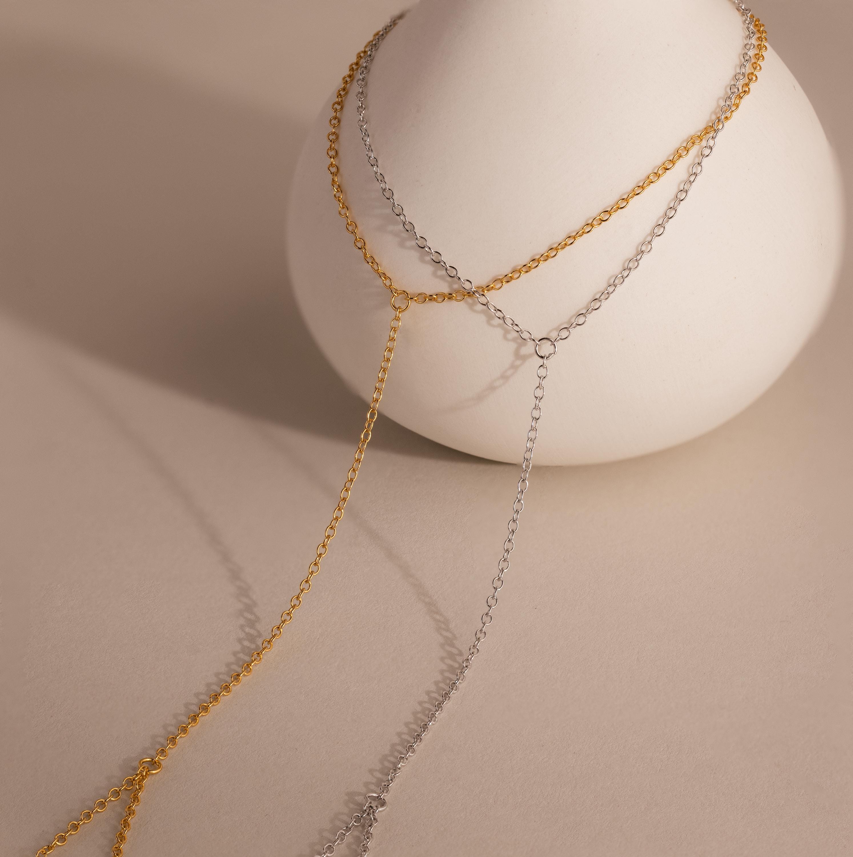 Two-tone dainty hand chain bracelets in gold and silver draped over a minimal ceramic vase, with delicate chain strands creating elegant shadows on a neutral surface.