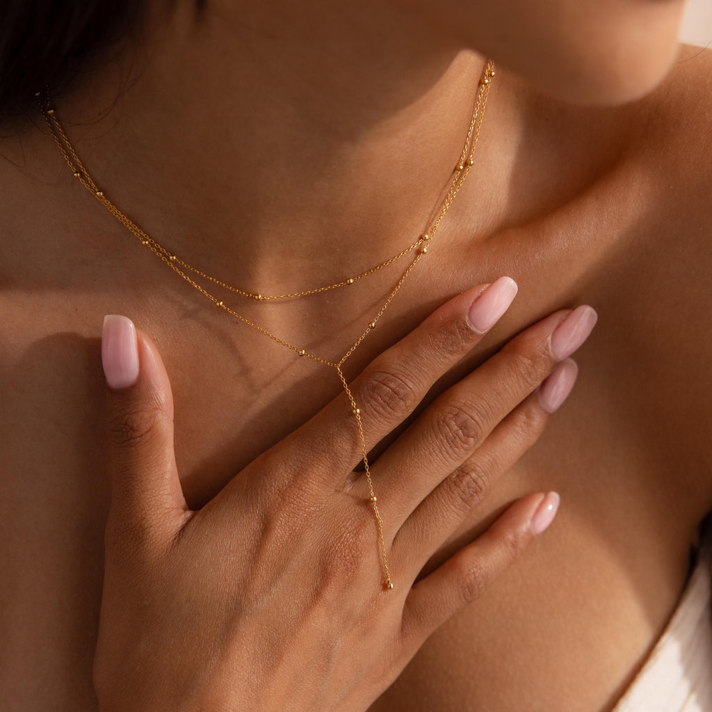 Detail of the gold lariat necklace draped over a woman’s hand and chest, highlighting the dainty bead accents.