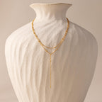 Gold satellite lariat necklace displayed on a sculptural ivory vase, showing full length and layered design.