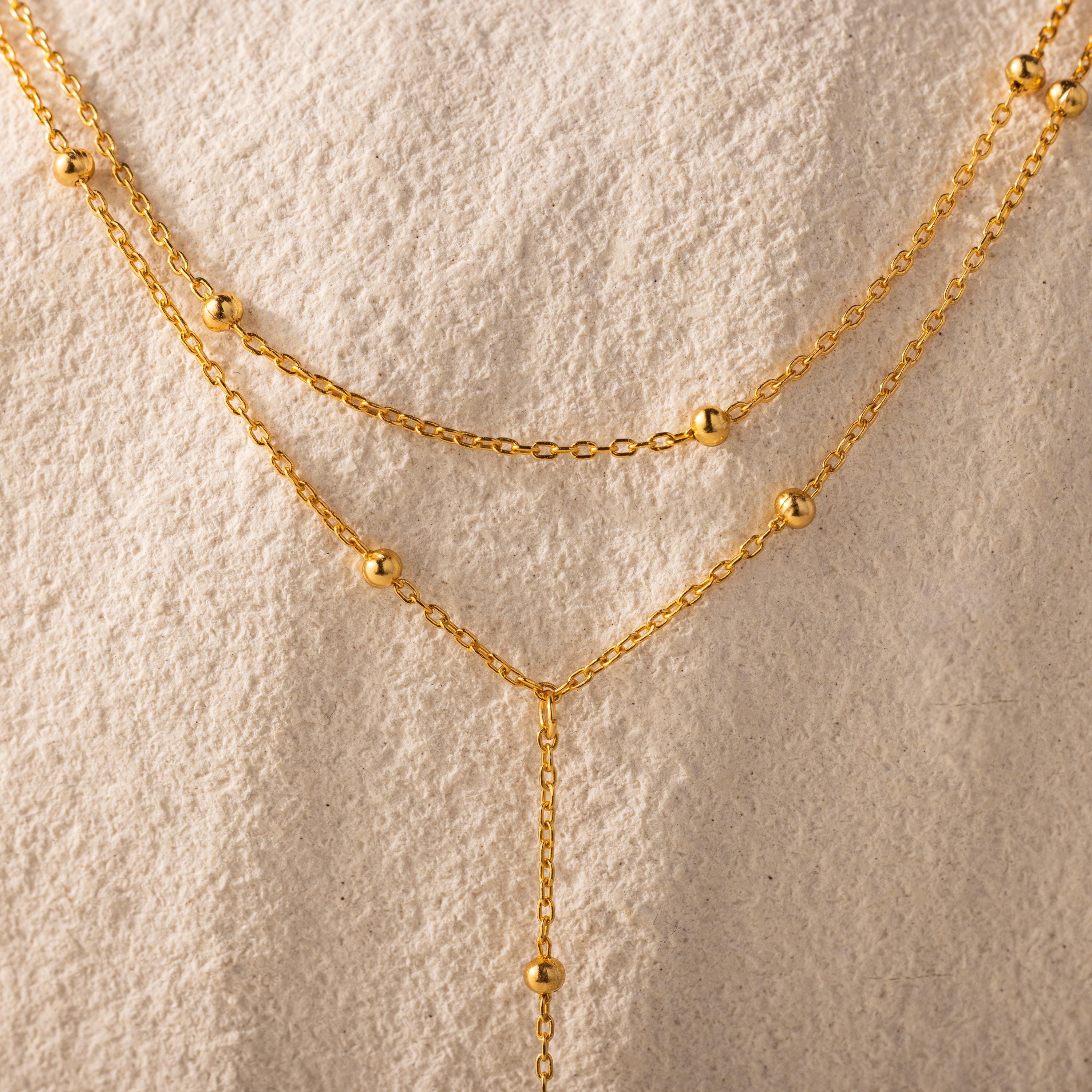 Close-up of the necklace’s gold satellite bead chain against a textured cream background.
