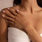 Close-up of a gold hand chain bracelet worn on a woman's hand, styled with multiple gold rings.