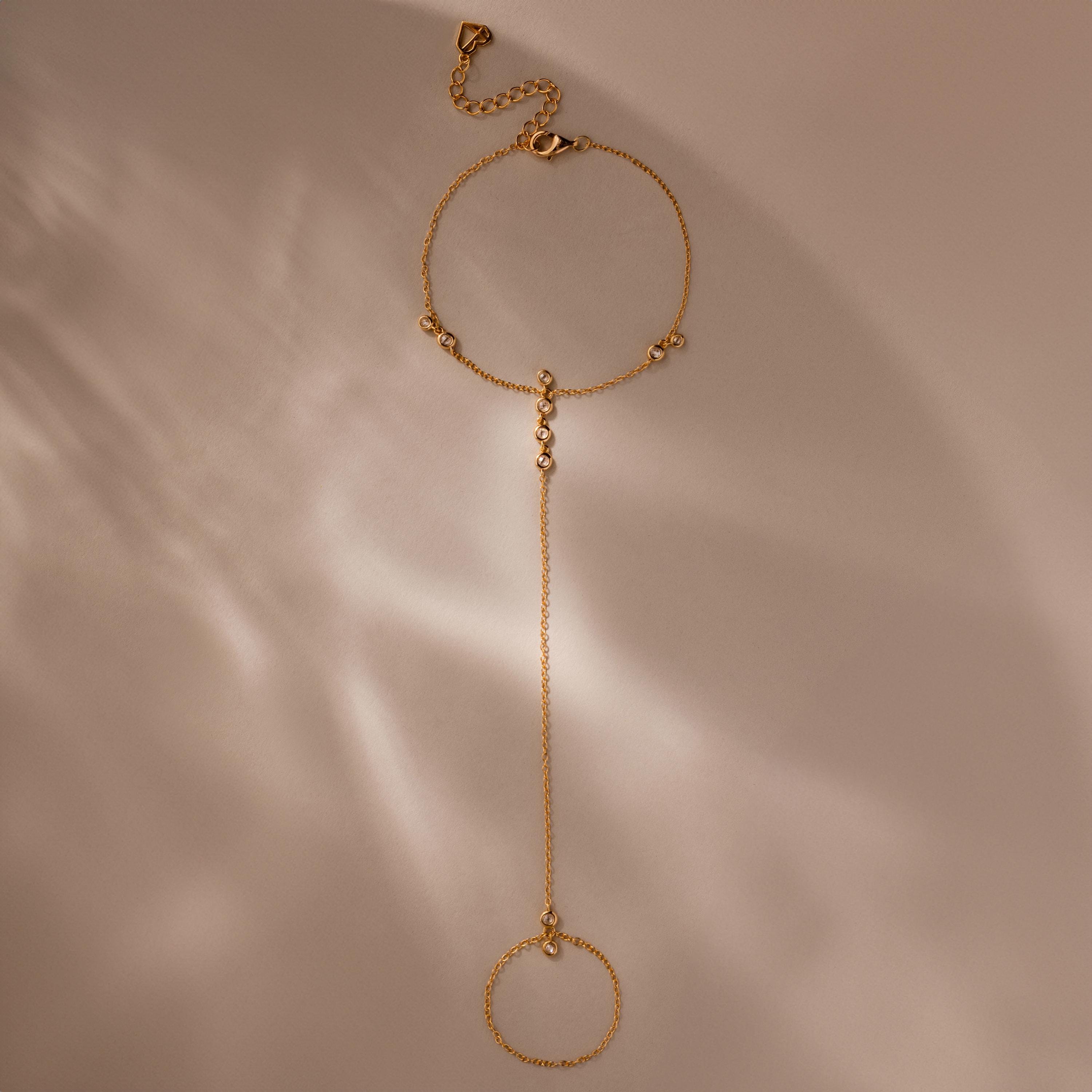 Flat-lay of a full gold hand chain bracelet with extension clasp, photographed on soft beige.