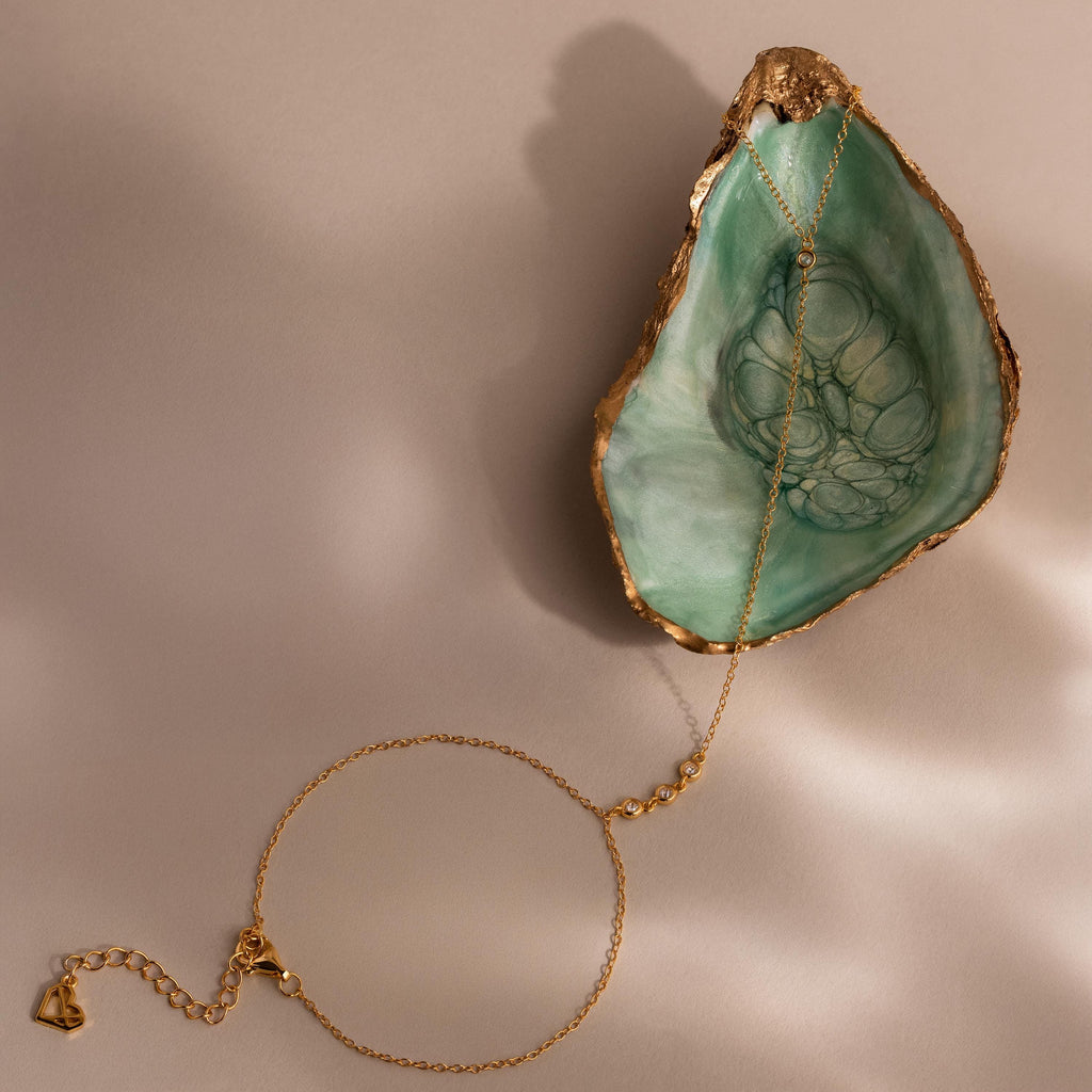 A gold Dainty Diamond Hand Chain Bracelet styled on a green seashell dish, showing the lobster clasp and extender chain.