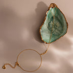 A gold Dainty Diamond Hand Chain Bracelet styled on a green seashell dish, showing the lobster clasp and extender chain.