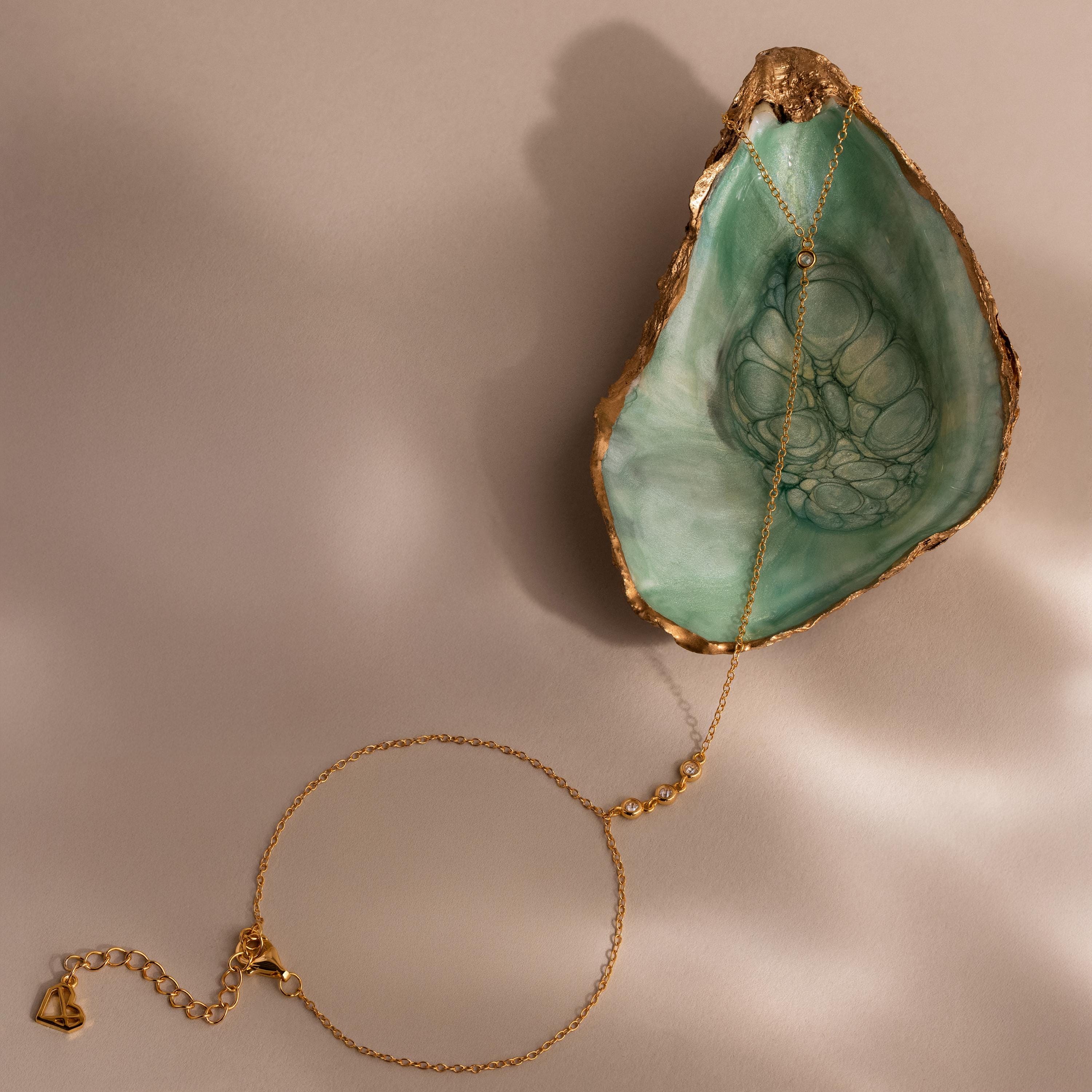 A gold Dainty Diamond Hand Chain Bracelet styled on a green seashell dish, showing the lobster clasp and extender chain.