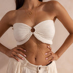 Model wearing a gold body chain draped over a white bandeau and cream pleated shorts.