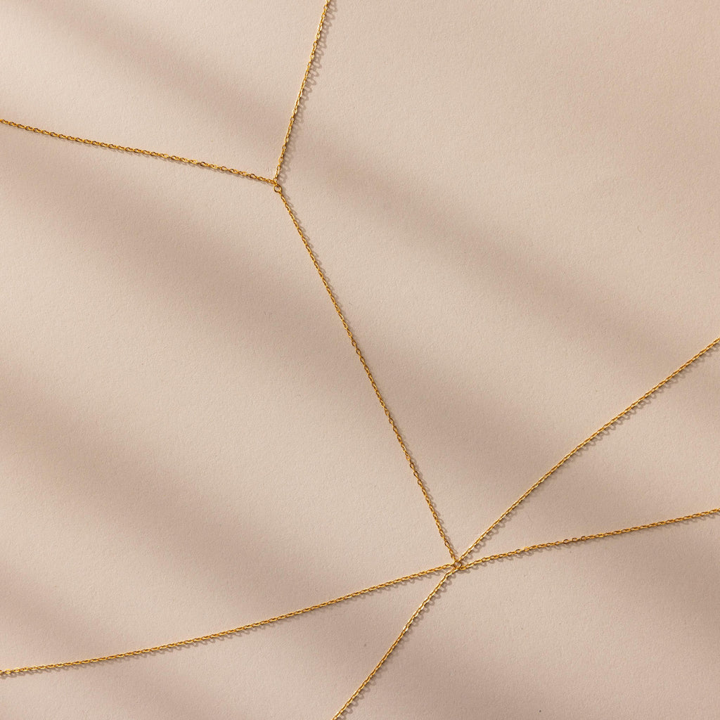 Close-up of gold body chain overlapping in delicate layers on a neutral background.