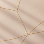 Close-up of gold body chain overlapping in delicate layers on a neutral background.