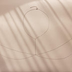 Silver body chain laid flat on a soft beige surface with shadow lines.