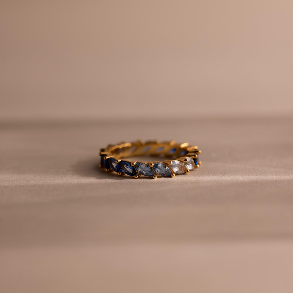 Gold eternity band set with marquise cut stones in a gradient of deep navy to soft icy blue, arranged in an ombré effect. Each stone is held by delicate prongs, creating a continuous shimmer around the ring.