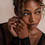 Model poses with hands gently resting on her face, wearing three gold rings including a marquise cut green ombré eternity band. The soft lighting and sheer black sleeves highlight the ring’s elegant sparkle.