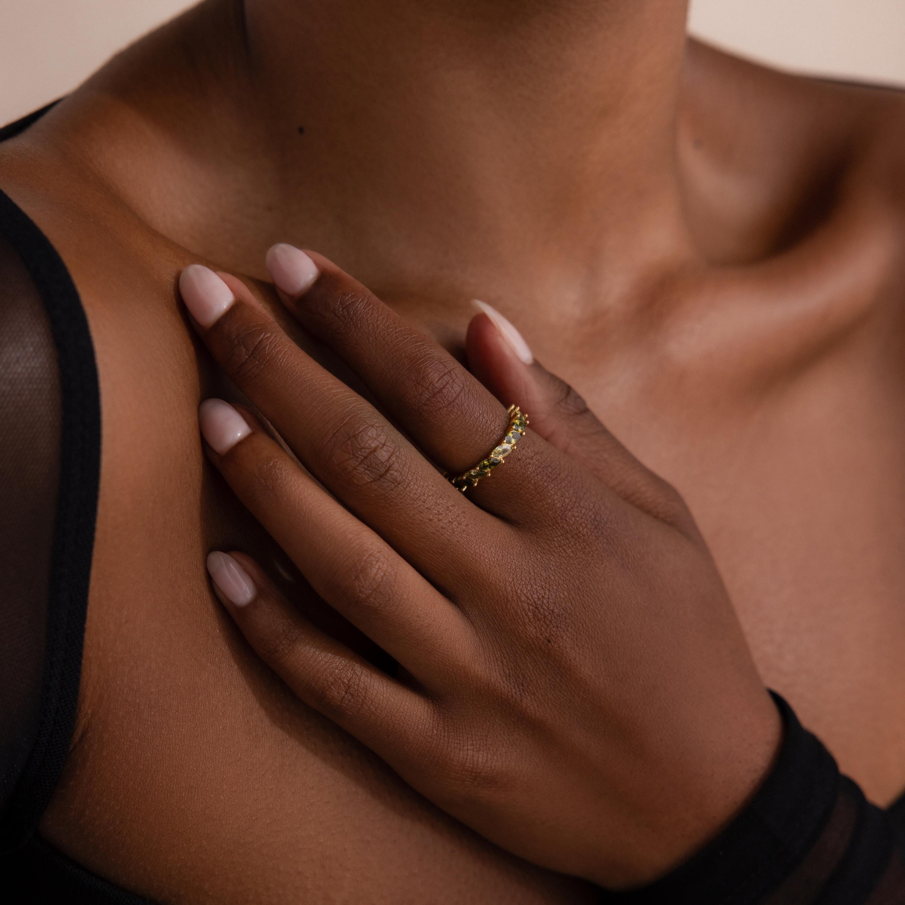 Close up of a hand resting on a collarbone, wearing a gold ring set with marquise cut green ombre stones. The ring contrasts elegantly against the model’s skin and sheer black sleeve.