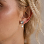 Side view of a model wearing a silver heart-shaped earring with bead detailing and a hanging pearl drop.